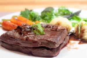 Angus iron flank steak mit gegrillten Möhren und Kartoffelnocken auf Teller in Nahaufnahme