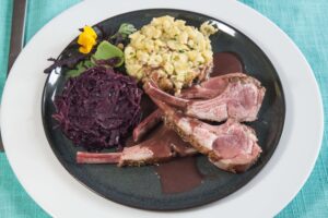 Lammkarree-mit-Baerlauchspaezle-und-Rotkohl-in-dunkler-Sauces-auf-shwarzen-Teller