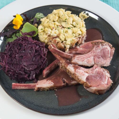 Lammkarree-mit-Baerlauchspaezle-und-Rotkohl-in-dunkler-Sauces-auf-shwarzen-Teller