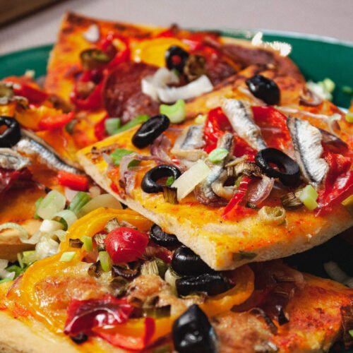 Spanische-Pizza-mit-GEmuese-und-Salami-belegt-auf-gruenem-Teller