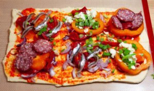 Spanische-Pizza-mit-Gemuese-und-Salami-belegt-auf-frischem-Teig