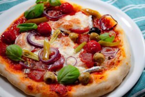 Pizzateig 7 https://oxbe.de/wp-content/uploads/2023/01/download.png Fertige-Salamipizza-mit-Zwiebeln-Mozerella-Paeperoni-und-Cherrytomaten-auf-weissem-Teller-