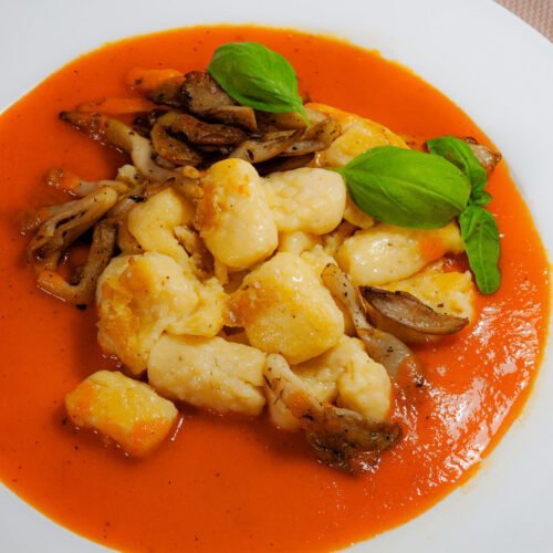 In-Butter-gebraeunte-Gnocchi-auf-Paprikasauce-mit-austernpilzen-und-frischen-BAsilikum-in-weissem-Telle