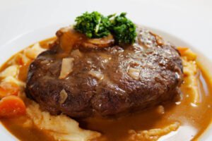 Klassisches Ossobuco mit Gremolata Kartoffelpueree und dunkler Sauce auf weissen Teller -2