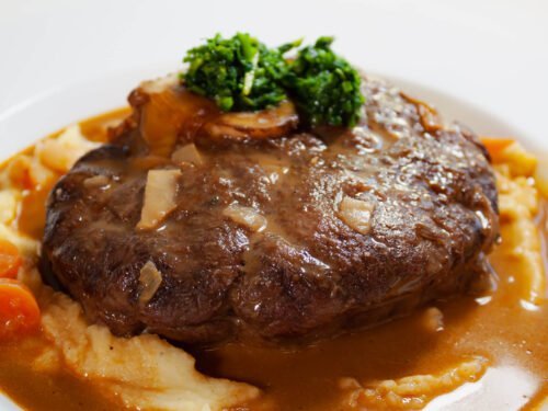 Klassisches Ossobuco mit Gremolata Kartoffelpueree und dunkler Sauce auf weissen Teller -2