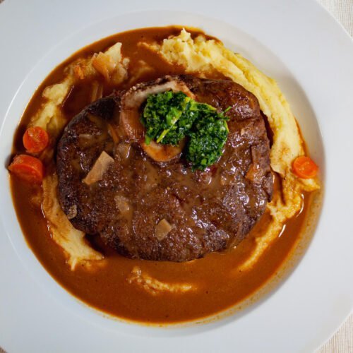 Klassisches-Ossobuco-mit-Gremolata-Kartoffelpueree-und-dunkler-Sauce-auf-weissen-Teller
