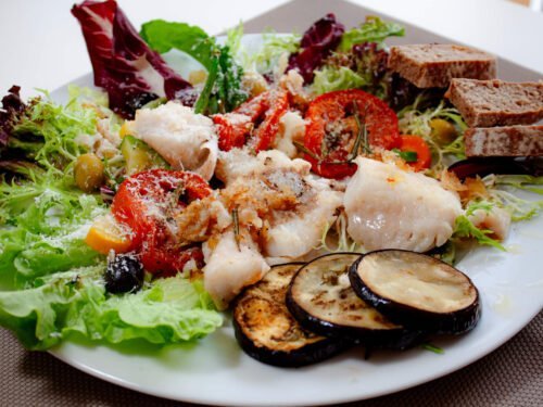 Mediterranen Salat mit Rotbarschfilet, gebackenen Tomaten und Auberginen auf Balttsalat mit Vollkornbrot auf weissem Tel