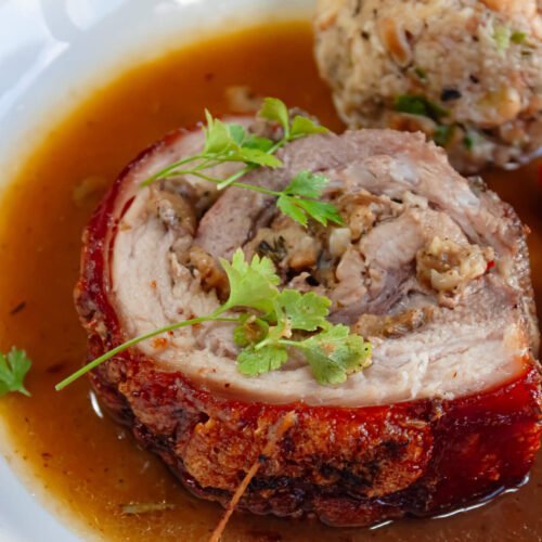 Porchetta-in-Duckler-Sauce-und-Brezenknoedel-auf-Weissem-Teller-