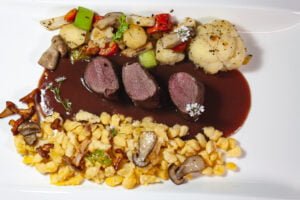 Wildhasenrücken auf weissem Teller mit Späzle geröstetem Wurzelgemüse und Pilzen