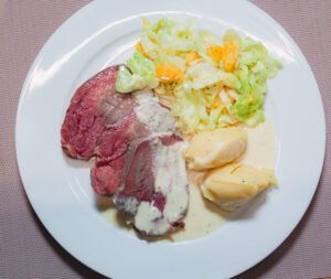 Rinderzunge in mit orangekohl kartoffelpüree und merretich shanesauce auf weissem teller